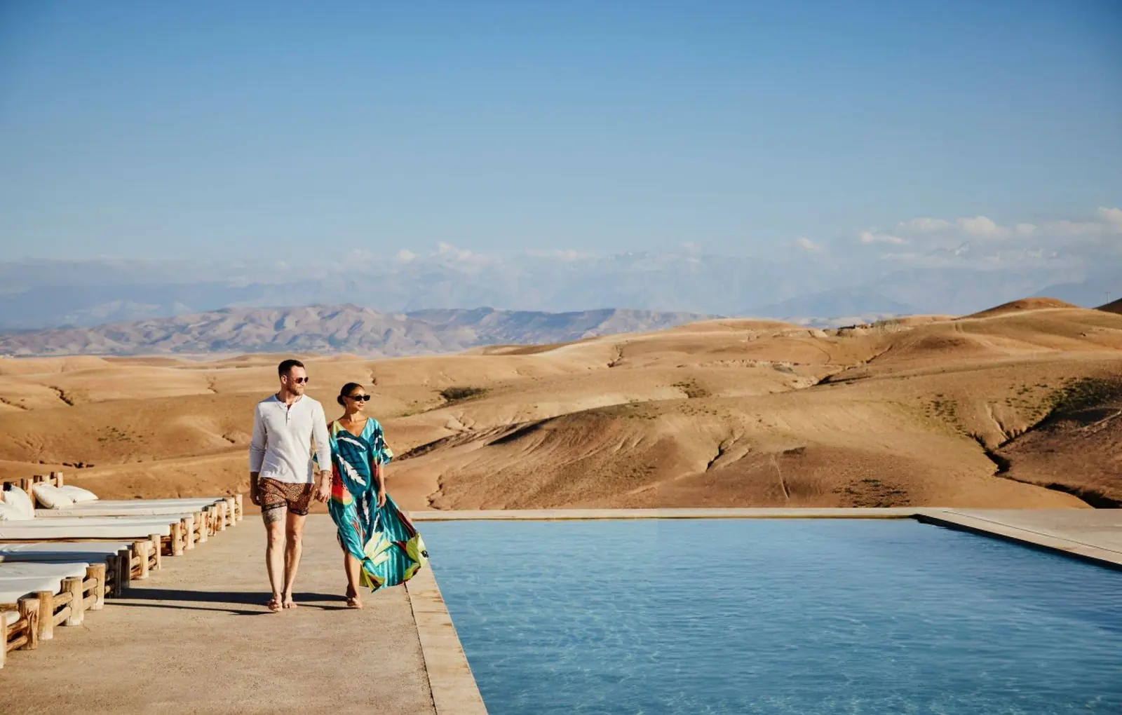A couple walking beside a pool at a camp in the Agafay Desert
