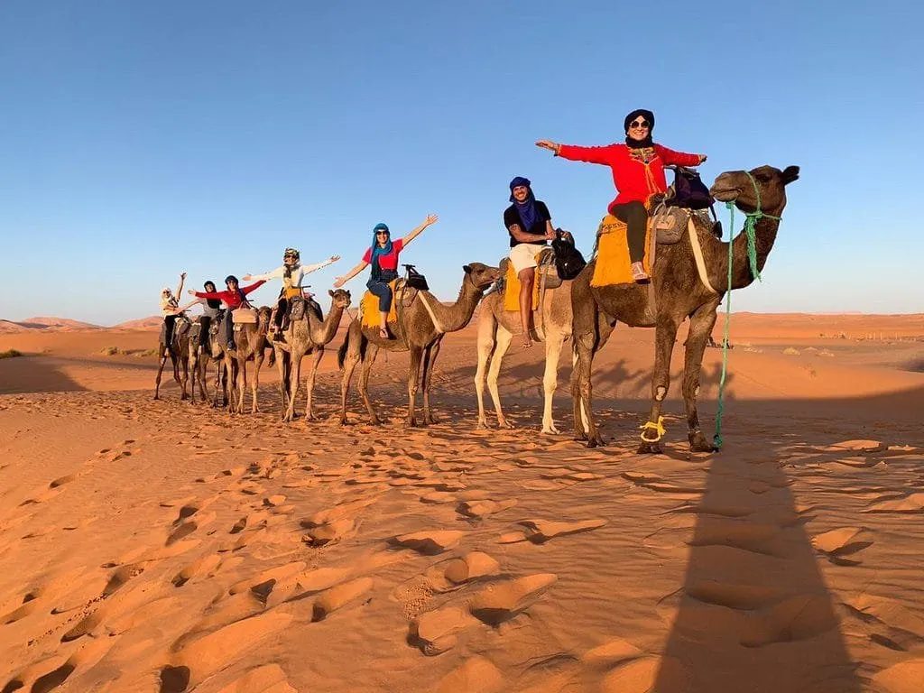 Travellers riding a camel caravan across orange dunes