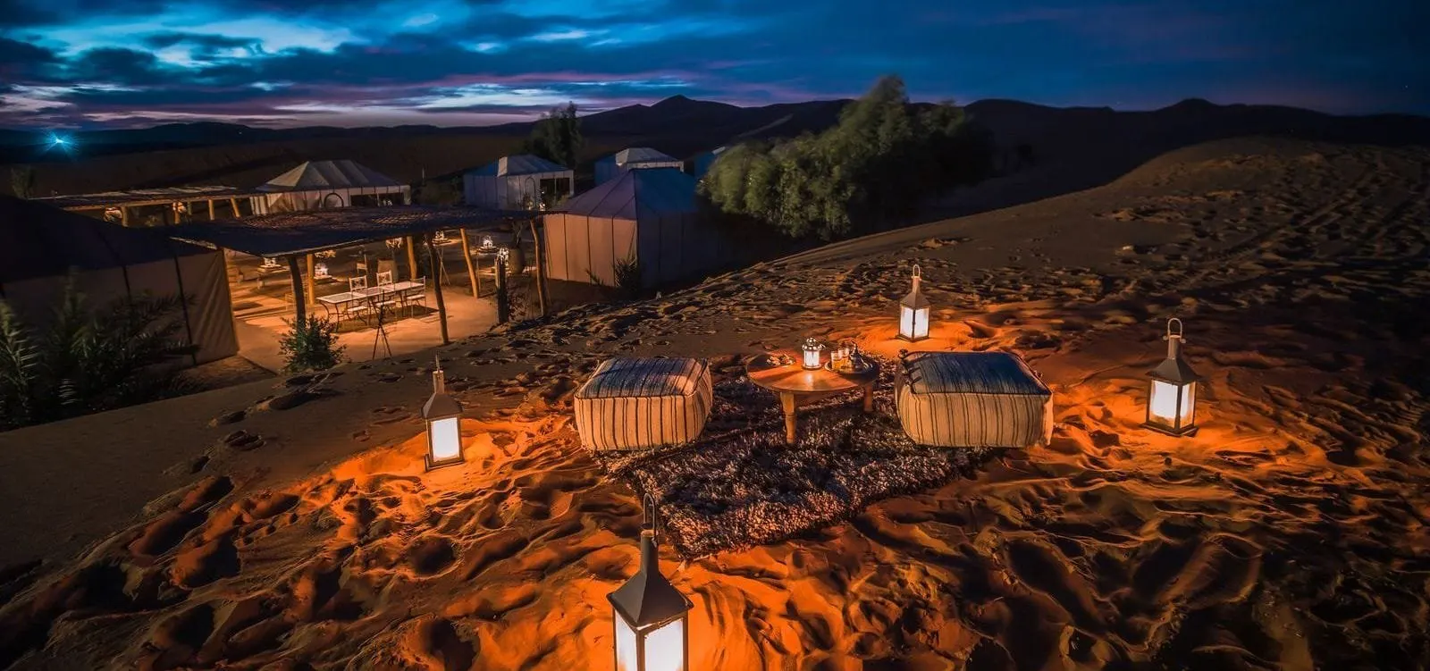 A desert camp lit by lanterns among the dunes at night