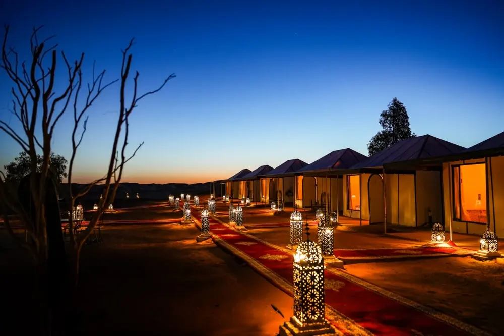Lantern-lit path and tents of a desert camp at dusk
