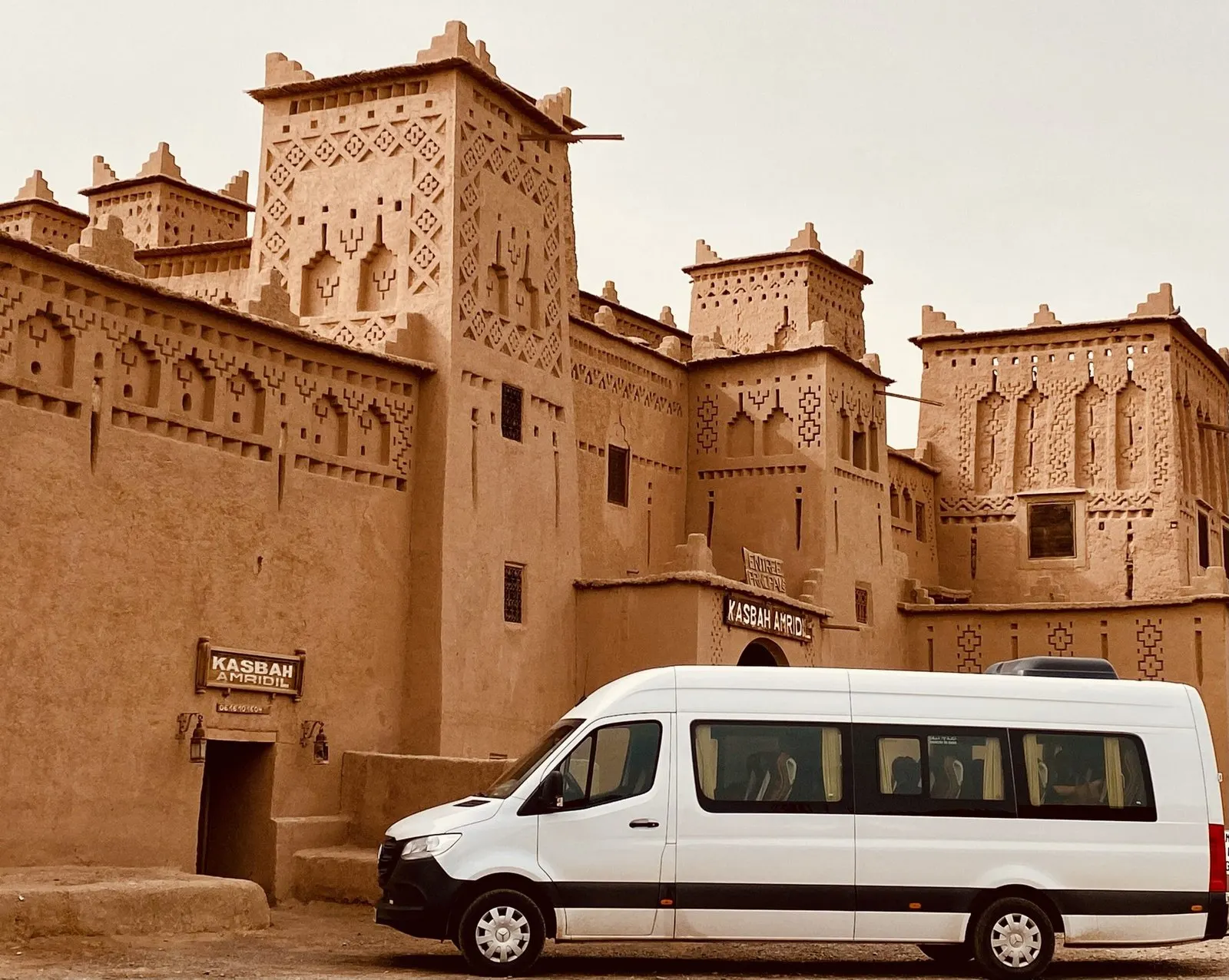 A tour minibus parked in front of an earthen kasbah