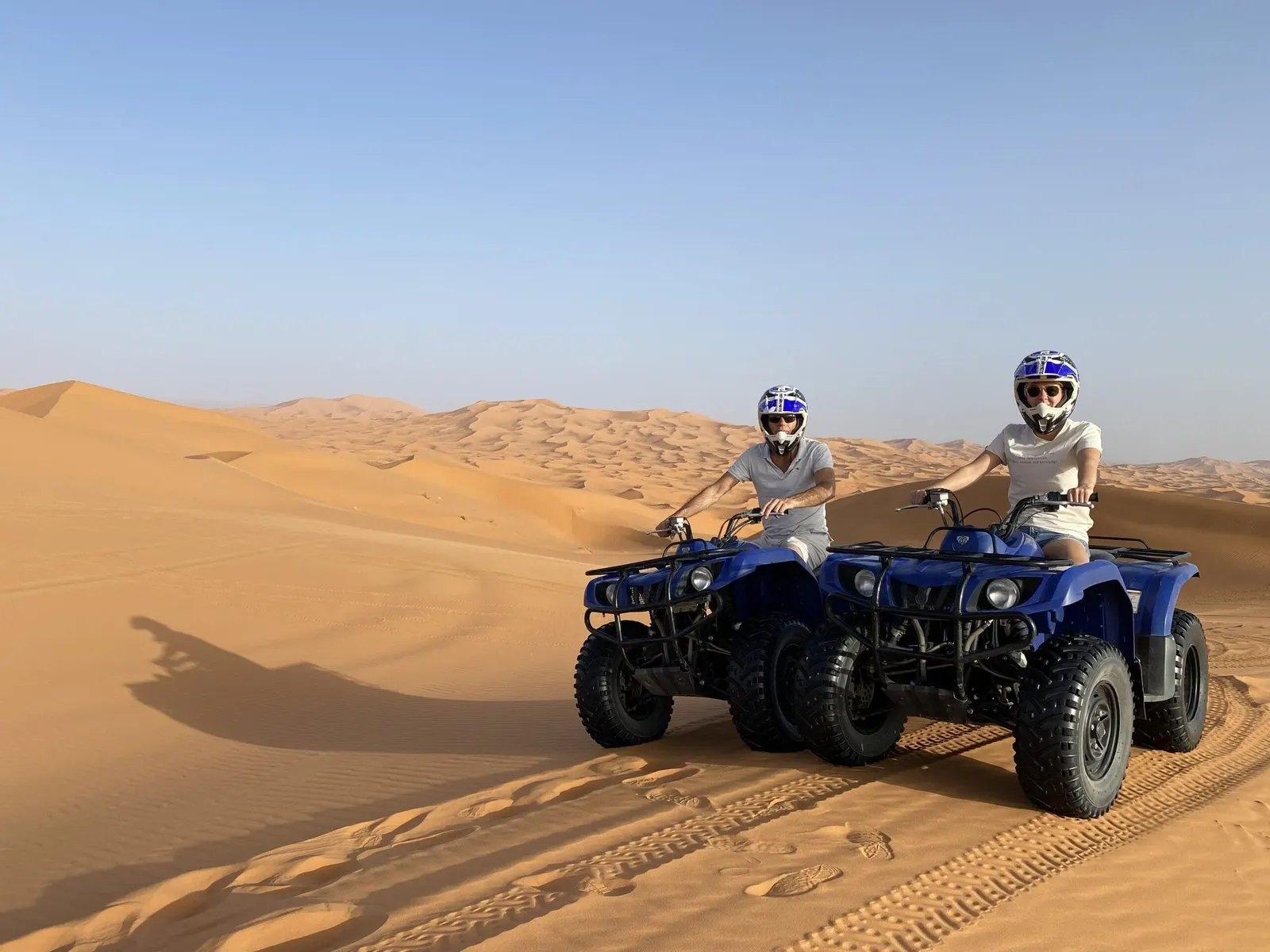 Two riders in helmets on quad bikes on the dunes
